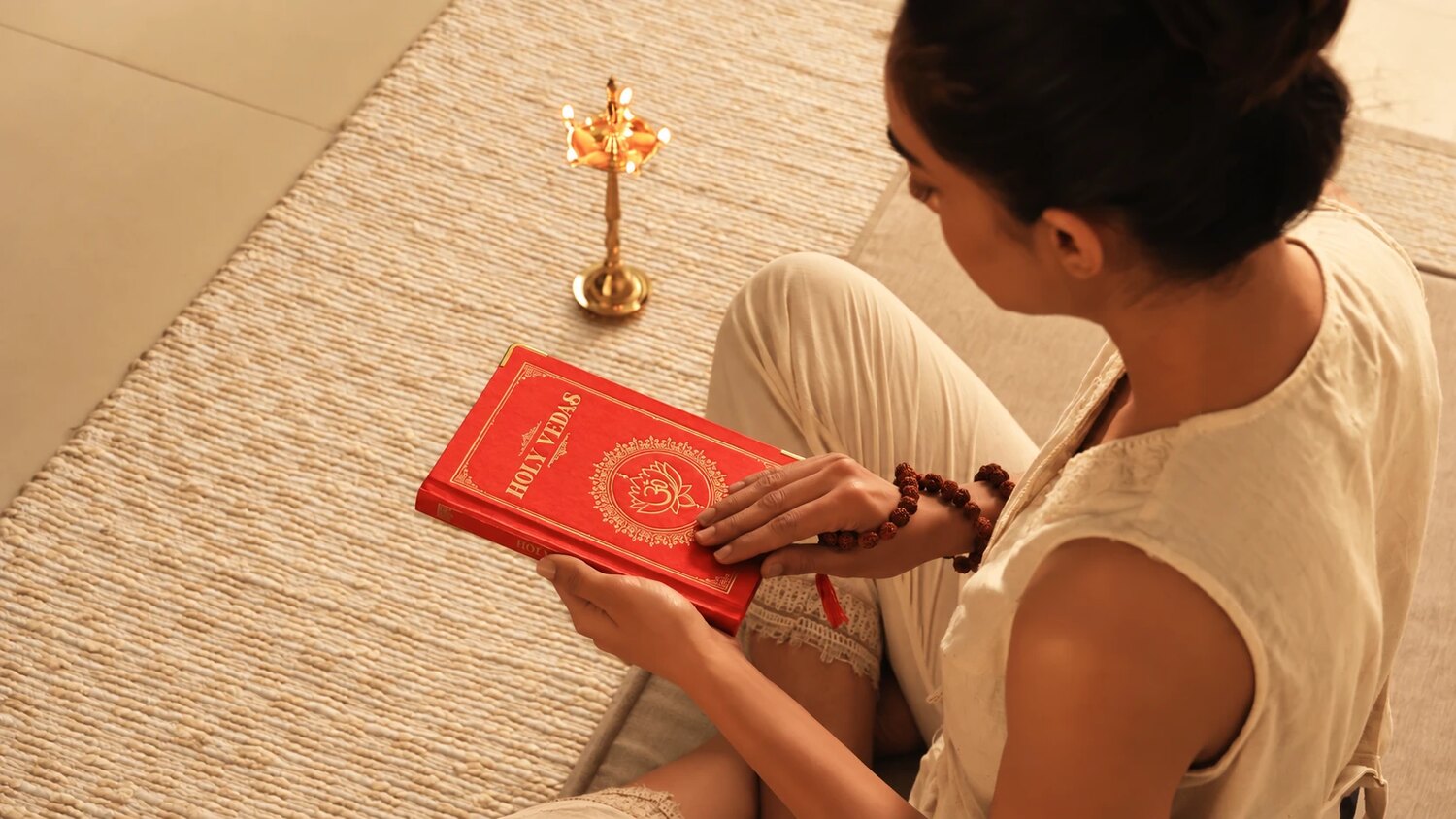 Femme assise sur une natte tressée, lisant un livre rouge des Vedas près d’une lampe à huile en laiton, pour Art of Vedas
